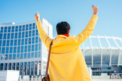 Rear view of man with arms raised standing against building