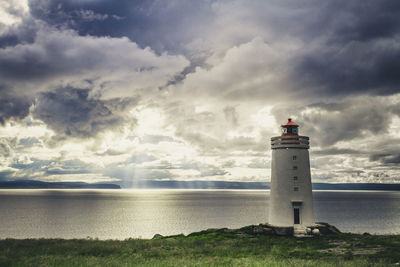 Lighthouse on beach against cloudy sky
