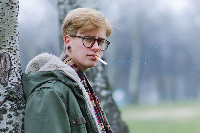 Portrait of man smoking cigarette while standing against tree