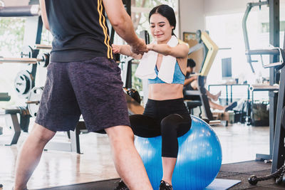 Midsection of instructor assisting woman in exercising at gym