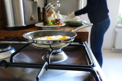 Fried egg in pan on stove while woman working in background at kitchen