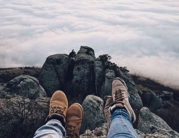 Low section of people on rock against cloudscape