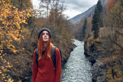 Young woman looking away while standing by trees during autumn