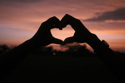 Silhouette hands forming heart shape against sky during sunset