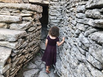 Rear view of girl walking amidst stone wall