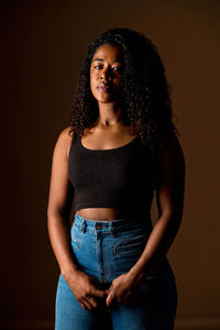 Portrait of young woman standing against yellow background