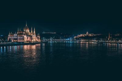 Illuminated city by sea against sky at night