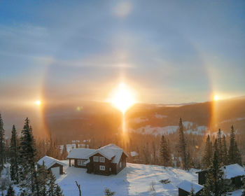 Cars on snow covered landscape against sky during sunset