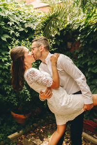 Newly wed couple kissing against plants