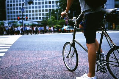 Low section of woman standing with bicycle on street in city