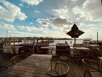 Empty chairs and tables by sea against sky