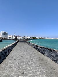 Footpath by sea against clear blue sky