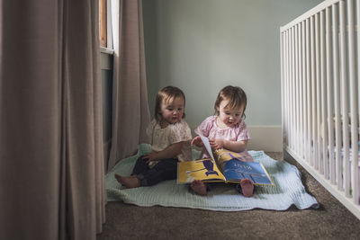 Portrait of twin toddler girls reading a book in window light