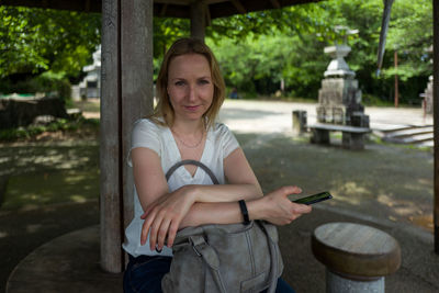 Portrait of woman sitting on seat by wooden pole