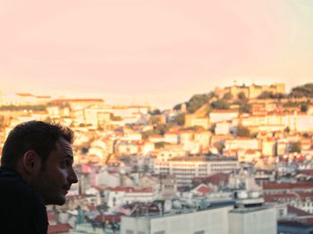 Man looking away against houses in city during sunset