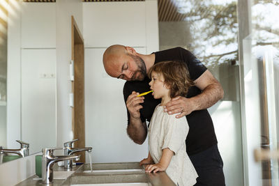 Father brushing son's teeth in bathroom