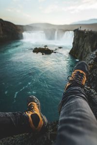 Low section of man sitting on mountain against waterfall