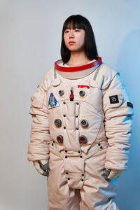 Serious young asian woman in spacesuit with dark hair looking away while standing under blue light before space mission against gray background