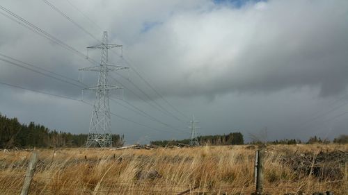Electricity pylon on field against cloudy sky