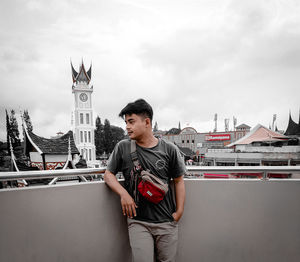 Young man standing on building against cloudy sky