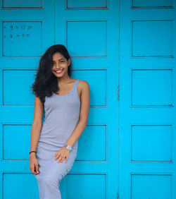 Smiling young woman standing against blue door