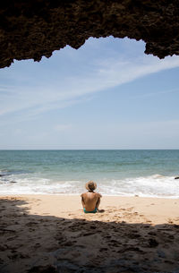 Rear view of shirtless man sitting on beach