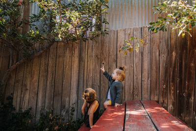 Two girls sitting on a red picnic table under an apple tree in the sun