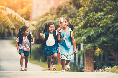 Happy friends walking with backpacks on road against plants