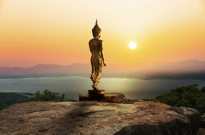 Statue on rock against sky during sunset