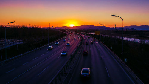 Vehicles on road against sky during sunset