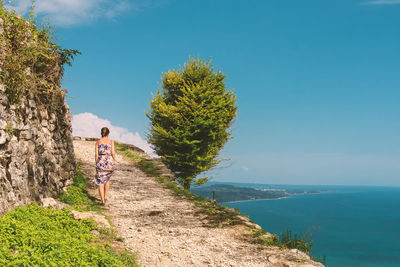 Rear view of woman walking on cliff against blue sky