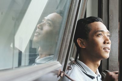 Close-up of smiling young man looking away against window