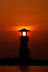 Silhouette lighthouse by sea against sky during sunset