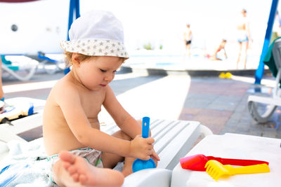 Small child in panama hat plays in the summer on sunny day near swimming pool