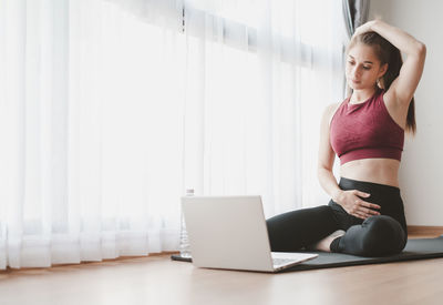 Young woman using mobile phone while sitting in laptop