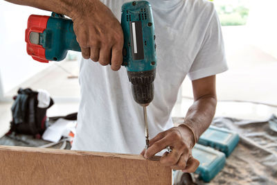 Midsection of man drilling wood in workshop