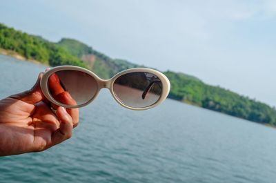 Cropped hand of person holding sunglasses over sea