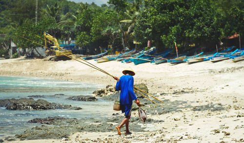 Rear view of fisherman walking on shore at beach