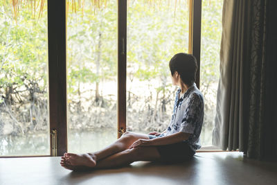 Side view of woman sitting on window at home