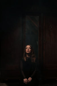 Portrait of beautiful young woman standing in dark room