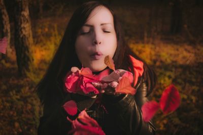 Close-up of young woman blowing autumn leaves