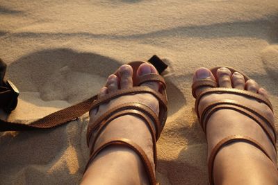 Low section of woman wearing sandals while sitting at beach