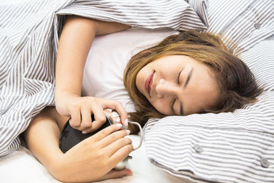 Woman holding alarm clock while sleeping on bed