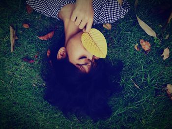 Directly above shot of woman with autumn leaf lying on field