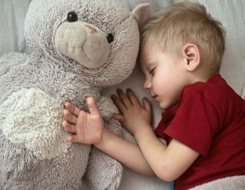 Close-up of boy sleeping with teddy bear on bed