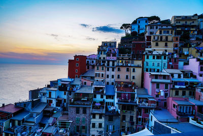 Buildings by sea against sky during sunset