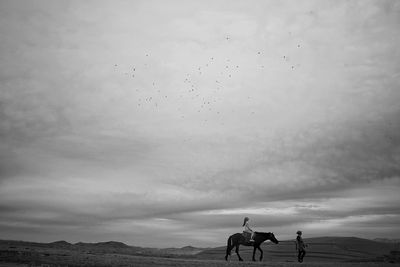 Woman riding horse on field against sky