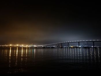 Illuminated bridge over river against sky at night