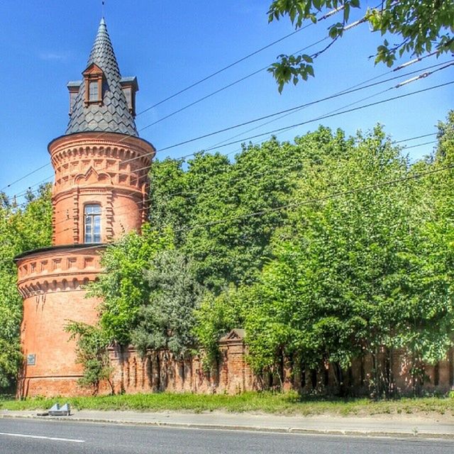 tree, architecture, built structure, building exterior, road, transportation, clear sky, street, sky, blue, the way forward, growth, green color, day, power line, outdoors, sunlight, low angle view, travel destinations, no people