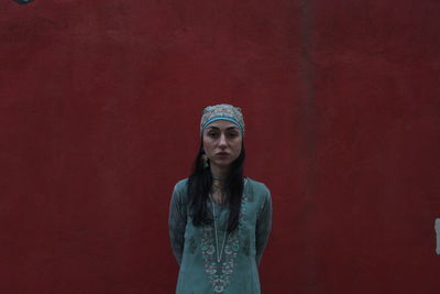 Portrait of young woman standing against red wall